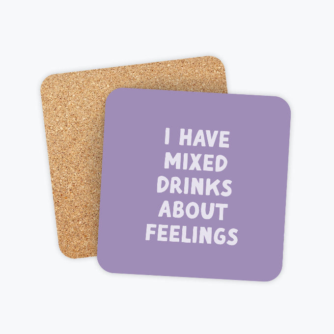 Two square cork coasters with rounded corners, one in natural tan cork and one in lavender purple with the white text 'I HAVE MIXED DRINKS ABOUT FEELINGS', shown on a light gray background.