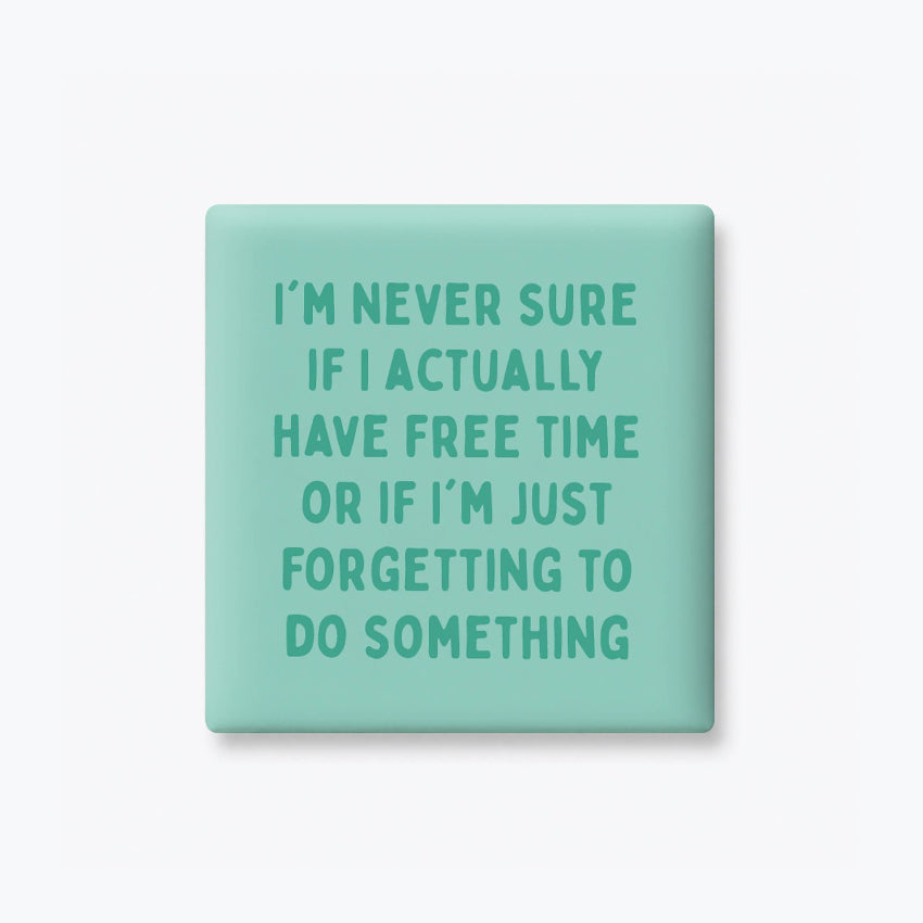 A square mint green pin badge with rounded corners featuring the humorous quote 'I'M NEVER SURE IF I ACTUALLY HAVE FREE TIME OR IF I'M JUST FORGETTING TO DO SOMETHING' in a matching teal sans-serif font, shown on a clean white background.