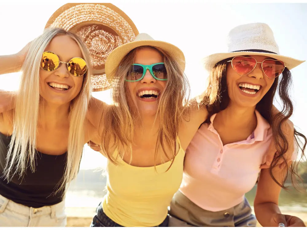 Three women on a girls trip wearing hats and sunglasses are posing together outdoors.