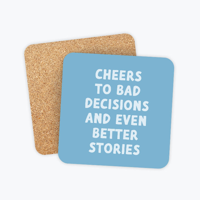 A set of two square coasters with rounded corners, featuring a light blue front coaster with white text that reads 'CHEERS TO BAD DECISIONS AND EVEN BETTER STORIES' and a natural cork backing, shown on a light gray background.