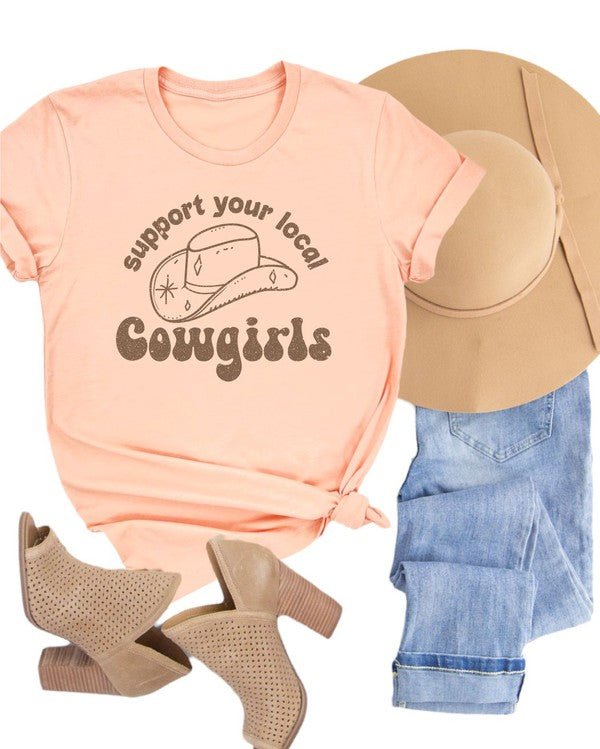 Pink t-shirt with 'Support your local cowgirls' text, beige boots, and denim shorts on a white background
